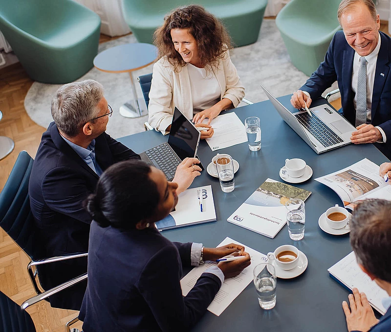 RAG Mitarbeiter*innen im Gespräch sitzen an einem Tisch mit Kaffee